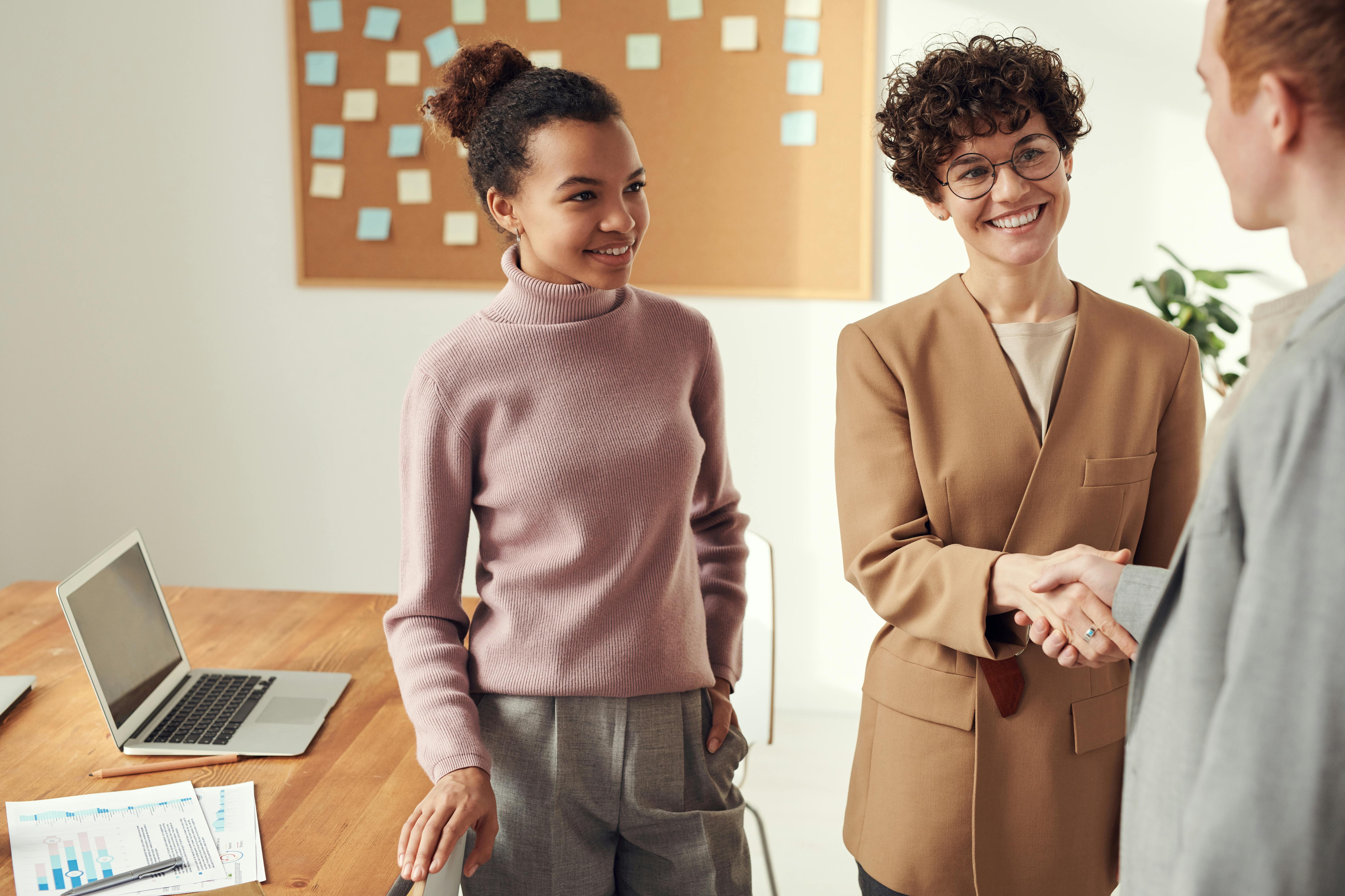 An image showing two professionals smiling and shaking hands during a business meeting, while a third person observes.